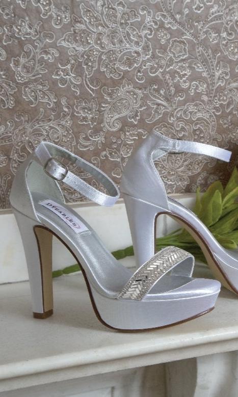 The Mary White Satin Prom Dress Shoes: Dyeables 4432 are silver high heels with ankle straps and a woven detail on the front strap, displayed against a patterned background.